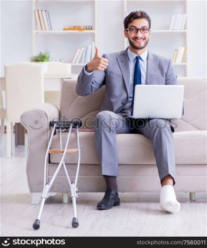 The businessman with crutches and broken leg at home working. Businessman with crutches and broken leg at home working