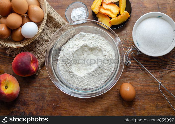 The cake ingredients and peach pie making on wooden table.