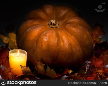 The candle burns before pumpkin with a maple leaf