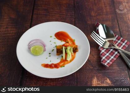 The canned sardine with tomato sauce and cooking ingredient was beautiful arrangement in white plate, stainless spoon and fork on napkin placed nearly on wooden table, copy space