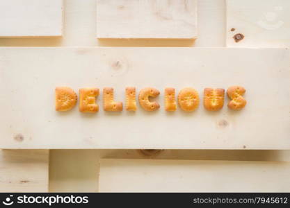 The capital letters word DELICIOUS. Alphabet cookie biscuits putting on piece of wood background.