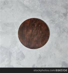 The central composition with brown wooden board on a gray concrete background, can be used for display or montage your products. A round wooden board on a gray stone background.