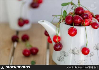 The cherries in white teapot on the wooden table.