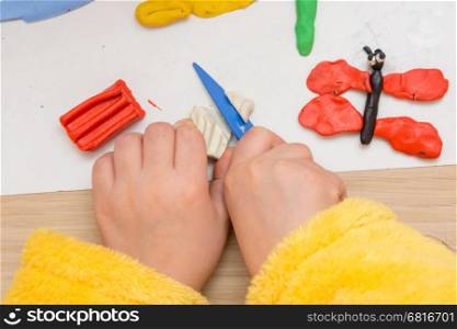 The child cuts off a piece of plasticine stack, close-up