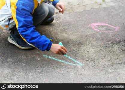 The child draws with chalk on the pavement. Children's creativity of the child in the warm season in the fresh air.