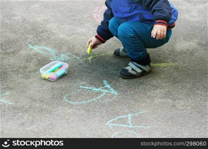 The child draws with chalk on the pavement. Children's creativity of the child in the warm season in the fresh air.