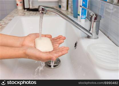 The child holds in his hands the soap on which water flows from the mixer