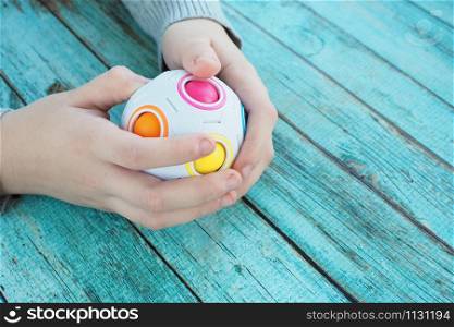 The child is busy with a puzzle in the form of a ball with colorful balls inside on a blue wooden background.