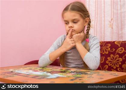 The child is thinking how to assemble a picture from puzzles