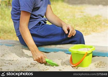 The child plays on the Playground in the warm season. The child is digging in the children's sandbox.