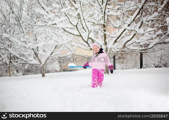The child plays with snow in the winter. A little girl in a bright jacket and knitted hat, catches snowflakes in a winter park for Christmas. Children play and jump in the snow-covered garden.. The child plays with snow in the winter. A little girl in a bright jacket and knitted hat, catches snowflakes in a winter park for Christmas.
