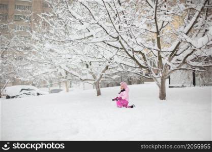 The child plays with snow in the winter. A little girl in a bright jacket and knitted hat, catches snowflakes in a winter park for Christmas. Children play and jump in the snow-covered garden.. The child plays with snow in the winter. A little girl in a bright jacket and knitted hat, catches snowflakes in a winter park for Christmas.