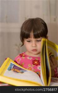 The child reading the book. The three-year girl in house conditions
