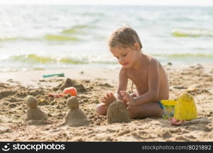 The child sits on the sandy beach of the reservoir and enthusiasm molds of sand cakes