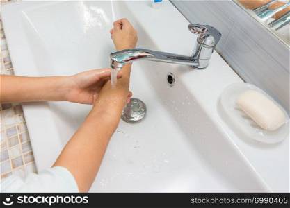 The child washes his hands up to the elbows in the bathroom sink