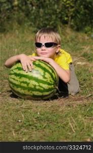 The child with a watermelon on a lawn in a wood