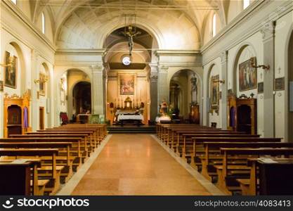 The Church of the Assumption of the Virgin Mary in the small village of Dozza near Bologna in Emilia Romagna: interiors: Cross, altar, desks, benches, paintings, candles