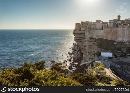 The citadel, wall and houses of Bonifacio in the south of Corsica perched on towering white cliffs and looking down on the evening sun glinting on the Mediterranean sea