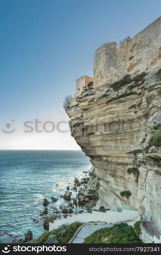 The citadel, wall and houses of Bonifacio in the south of Corsica perched on towering white cliffs and looking down on the evening sun glinting on the Mediterranean sea