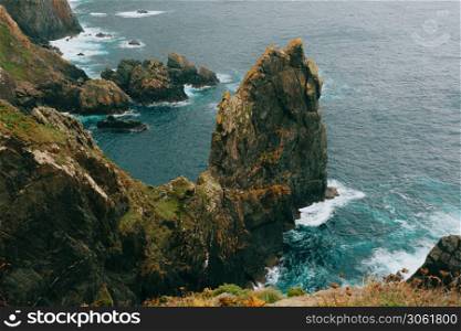 The cliffs and giant stones in europe with the wild ocean breaking against it on green and brown tones