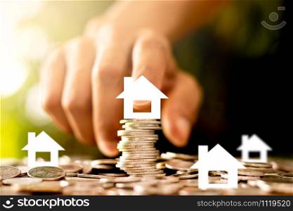 The coins are stacked and there is a white paper house on top. The men&rsquo;s hands are gently touching, the concept of saving money and growing financially.