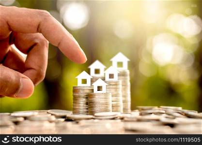 The coins are stacked in five rows and there is a white paper house on top. The men&rsquo;s hands are gently touching, the concept of saving money and growing financially.
