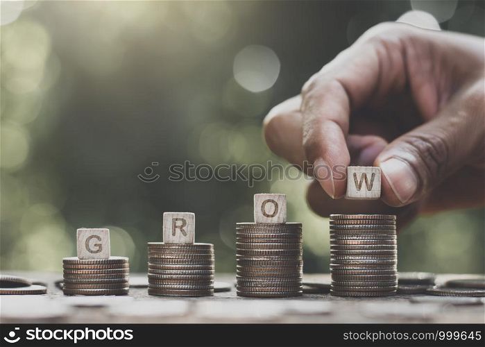 The coins are stacked on an old wooden table with a man's hand picking the dice on top, financial growth ideas.
