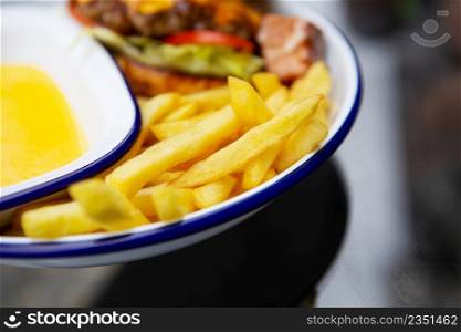 The concept of fast food. French fries lie on a meta plate along with cheddar cheese sauce and a hamburger in the background. The concept of fast food. French fries lie on a meta plate along with cheddar cheese sauce and a hamburger in the background.