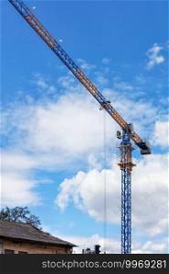 The concept of new development of residential areas of the city. An arrow of a tower crane over the roof of a dilapidated old house against the blue sky. Copy space.. An arrow of a tower crane against a blue sky, divides the image diagonally.