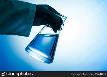 The conical flask with green liquid in the hand - laboratory glass. The conical flask