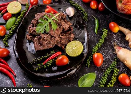 The cooked pork is on a black plate with tomatoes, peppers, and fresh pepper seeds, garlic, and Lime.