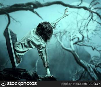 The corpse woman gets out of the computer monitor against the background of the moon and daed tree. Halloween.. The corpse woman gets out of the computer monitor
