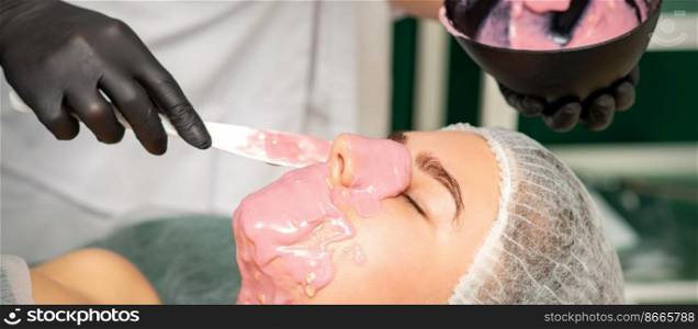 The cosmetologist applying an alginate mask to the face of a young woman in a beauty salon. The cosmetologist applying an alginate mask to the face of a young woman in a beauty salon.