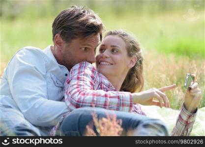 the couple lay on the grass and hold a smart-phone