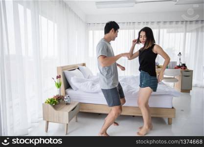 The couple put on their headphones and listened to music on their mobile phones on the couch and they were dancing happy in the house for social distance and self responsibility concept
