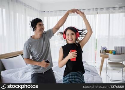 The couple put on their headphones and listened to music on their mobile phones on the couch and they were dancing happy in the house for social distance and self responsibility concept