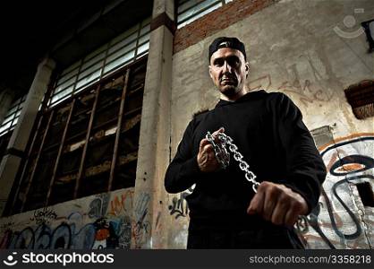 The criminal with threat holds in hands a chain in the thrown building
