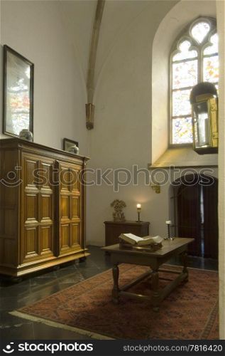 The cript of an ancient church with the holy bible on the table, and a burning candle in the background. Light shines through the stained window