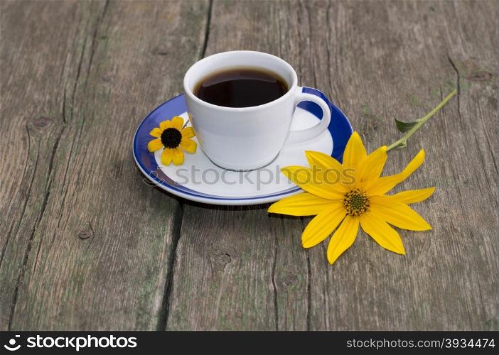 the cup of coffee on a wooden table decorated with two yellow flowers, a still life, a subject fall