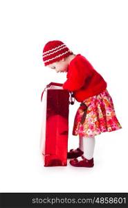 The curious little girl in the red dress looks in the red shopping bag isolated on white. The girl looks a gift