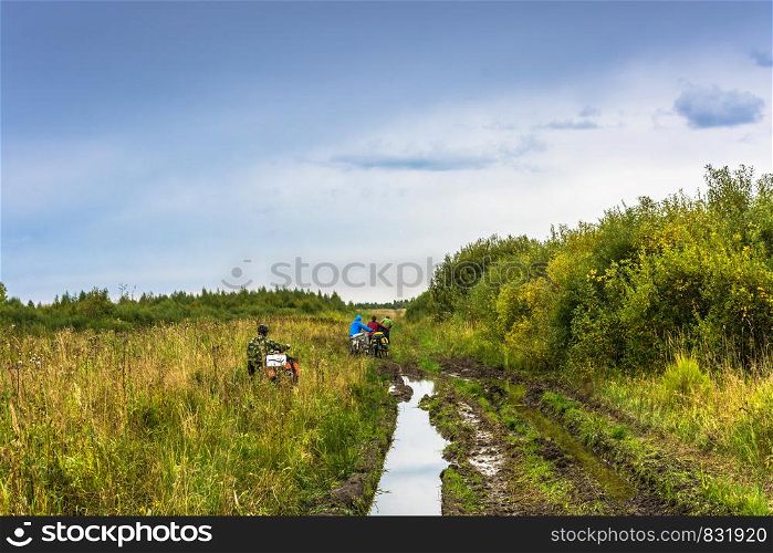The cyclists go through the high grass along the broken road of an autumn day.