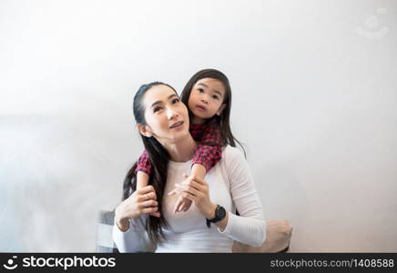 The daughter is hugging and playing with her mother and laughing and smile happy on the sofa while relaxing at home.
