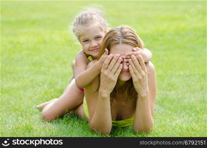 The daughter of fun mom closed her eyes while lying on a green lawn
