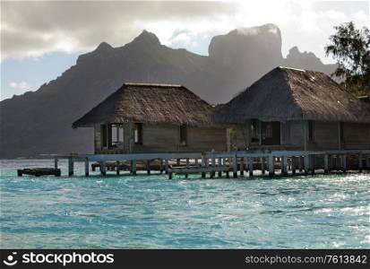 the destroyed thrown huts on water and island with palm trees in the ocean and mountains on a background