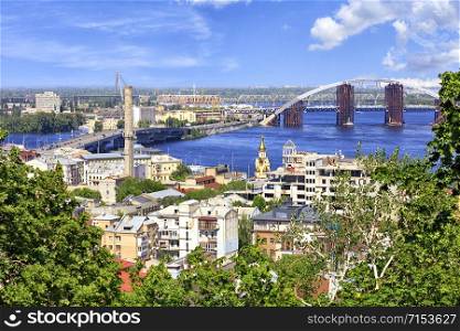 The Dnipro River with various bridges on a bright summer day and a view of the old Podol district of the city of Kyiv.. The landscape of the summer city of Kiev with a view of the Dnieper River, many bridges and the old Podol district.