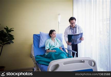 The doctor is explaining about the brain X-ray results to a female patient lying in bed at a hospital