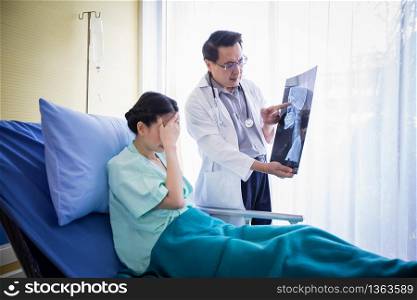The doctor is explaining about the brain X-ray results to a female patient lying in bed at a hospital