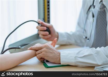 The doctor uses two fingers checking the pulse of a patient woman on the wrist and checking blood pressure with Mercury sphygmomanometer in the hospital. Medical and healthcare concept.