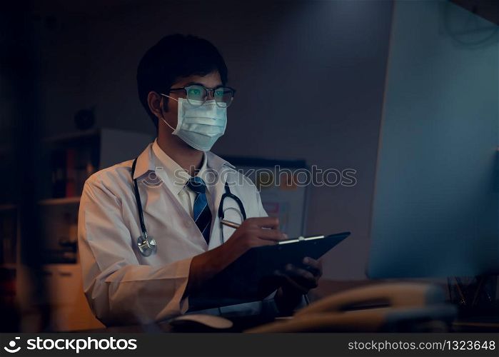 The doctor wearing mask is sitting at a desk at the night, Which is researching how to treat the patient?s condition.