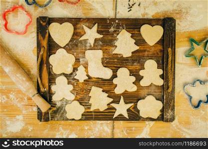 The dough in different forms cuted out by cookie cutters on wooden board, top view, nobody. Hearts, stars and gingerbread man, pastry templates on the table